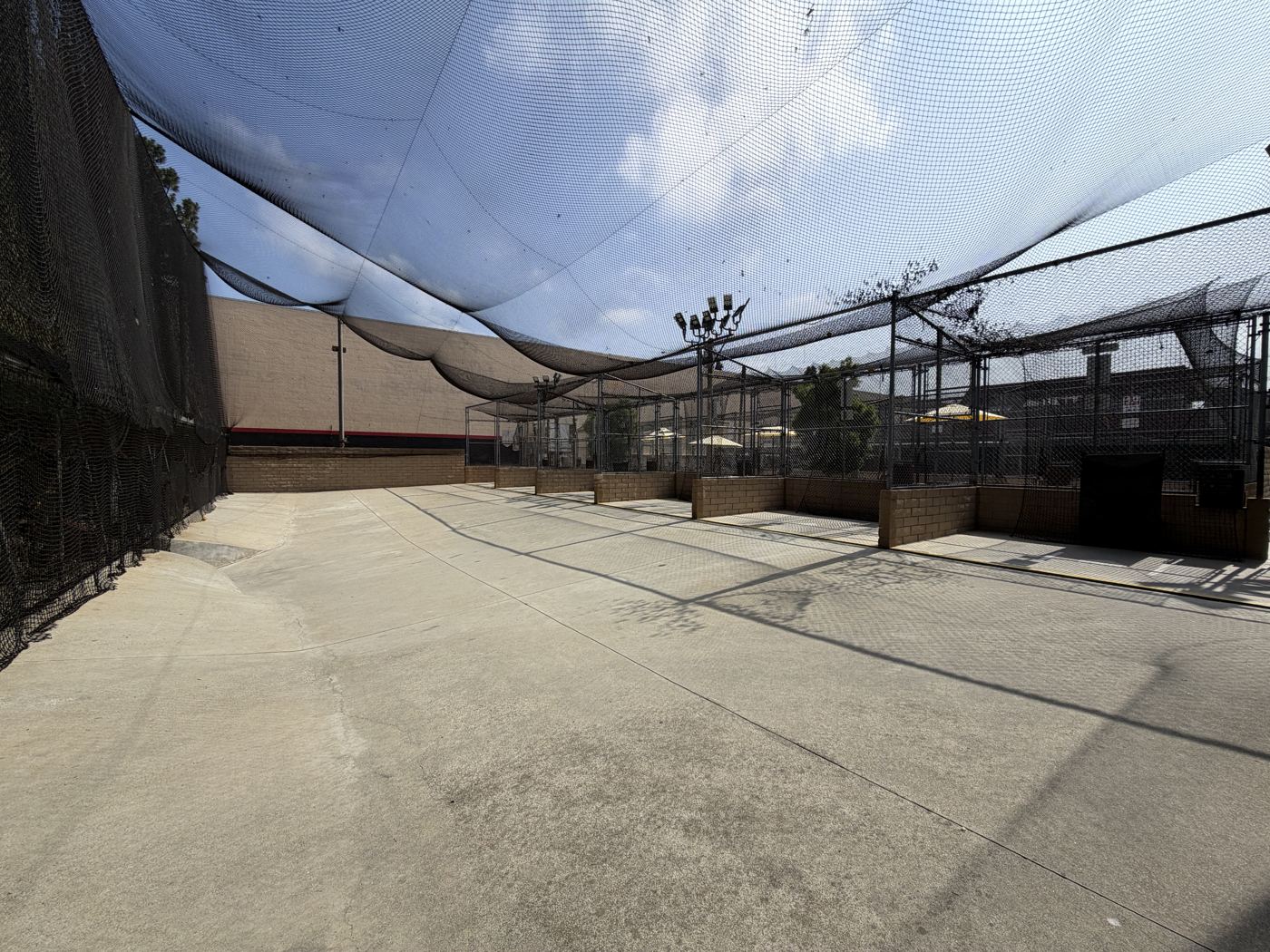Open-air batting area beneath the netting and blue sky