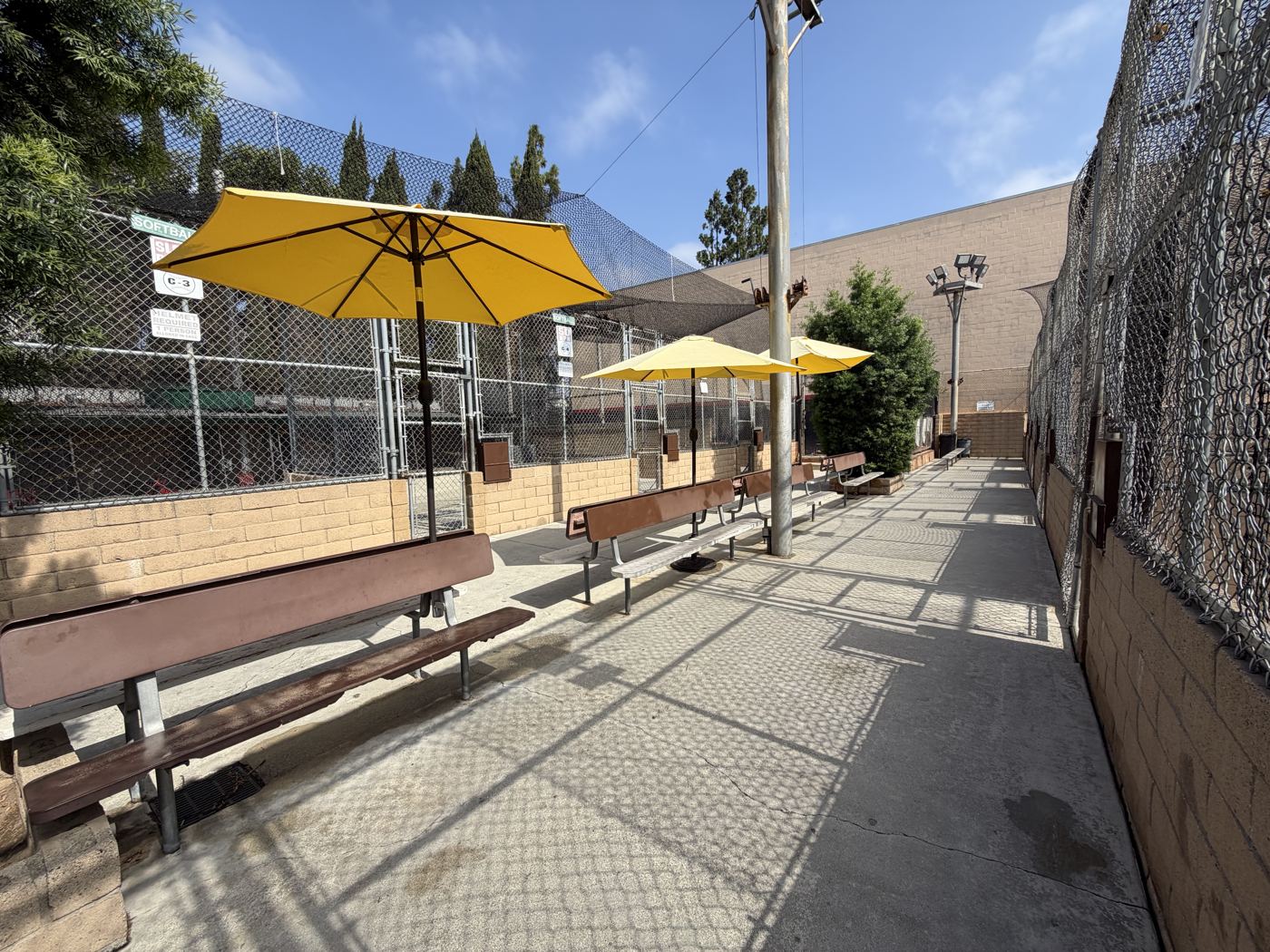 Shaded benches under yellow umbrellas beside the batting cages